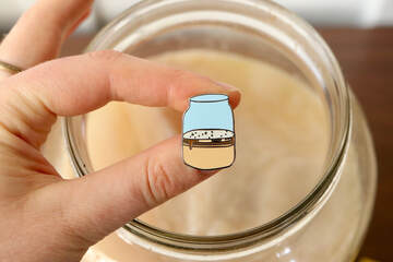 kombucha enamel pin of kombucha scoby in a jar in front of real jar of kombucha with SCOBY