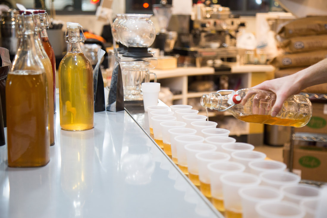 hand pouring rows of kombucha samples in cups