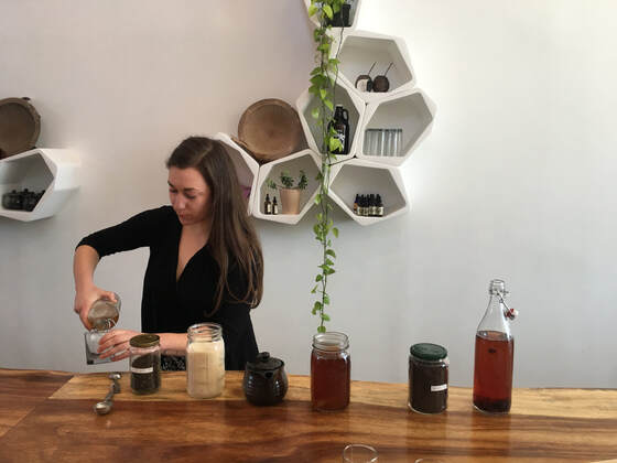 woman pouring kombucha into cup with tea, sugar and kombucha on a counter