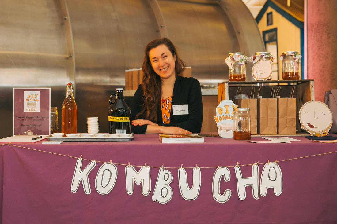 person sitting at kombucha brewing table serving homemade kombucha samples